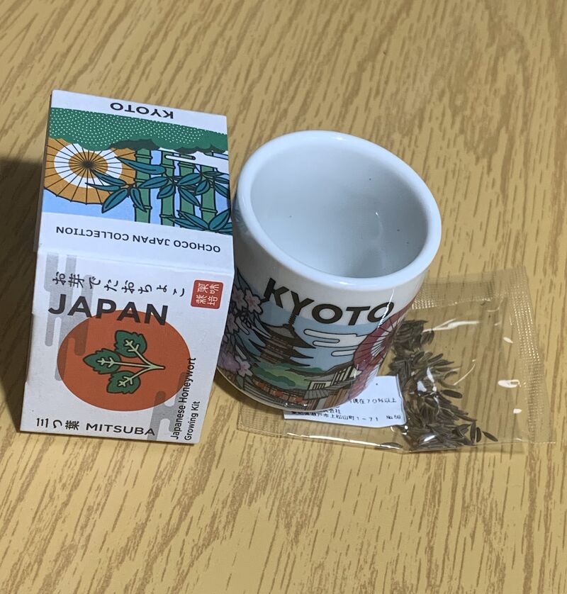 a sake cup with the word Kyoto on it. on the right is a bag of Japanese wild parsley and on the right is the outer paper packaging.
