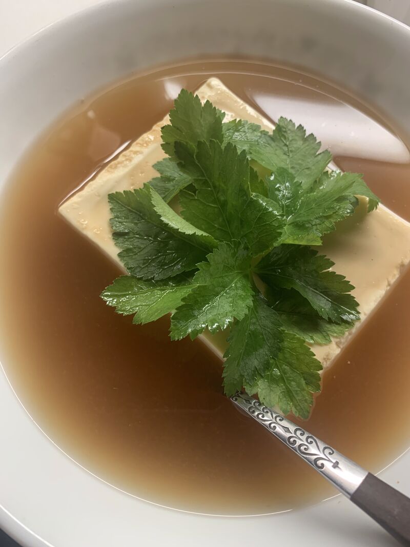 a bowl of miso soup with a block of tofu, topped with japanese wild parsley.